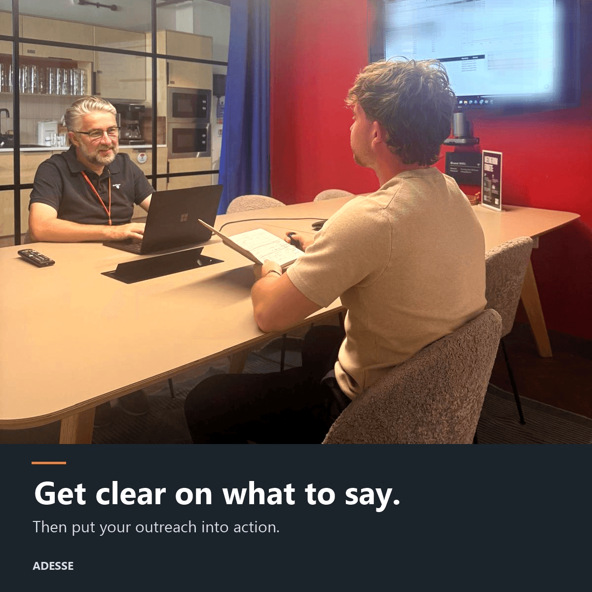 Two people working across a meeting table with a laptop and notes. Poster text: ‘Get clear on what to say. Then put your outreach into action. ADESSE.’