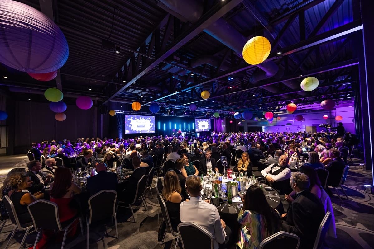Guests seated at round tables in an event hall with colourful hanging lanterns.